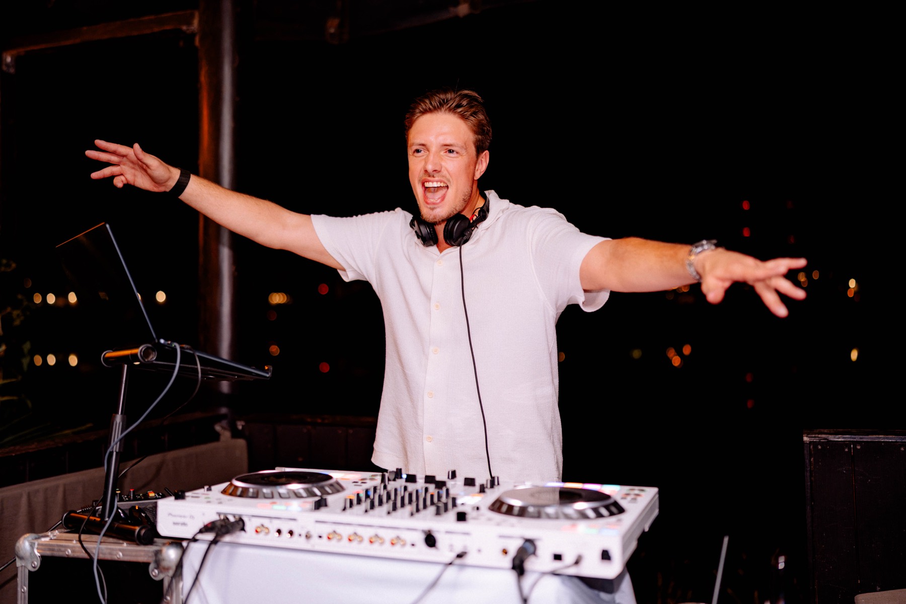 DJ mit weit ausgebreiteten Armen hinter dem weißen Controller, dahinter die dunkle Nacht